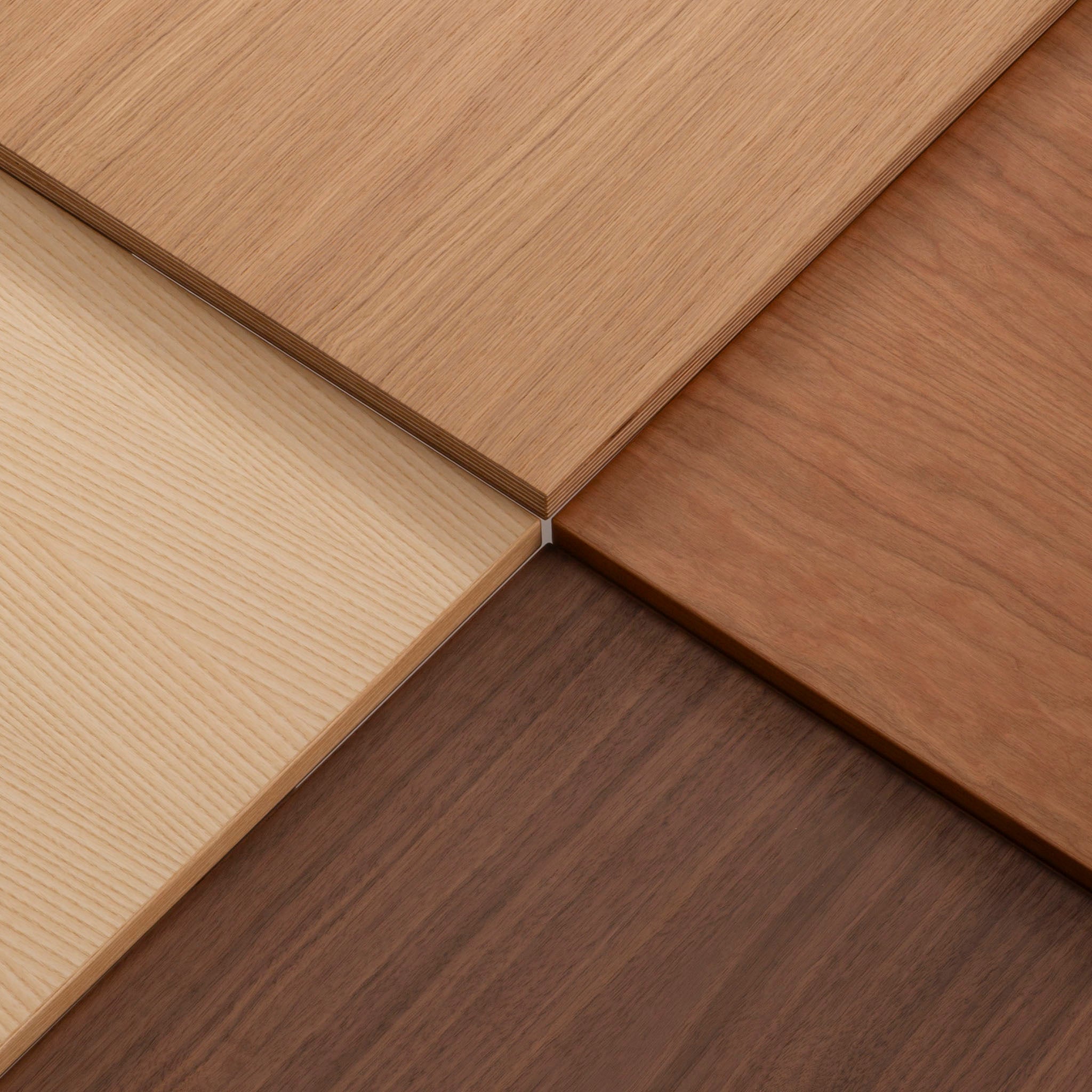 Vier Holzplatten in verschiedenen Farbtönen und Maserungen treffen in der Mitte aufeinander und bilden eine geometrische Anordnung mit kontrastierenden hellen und dunklen Brauntönen.
