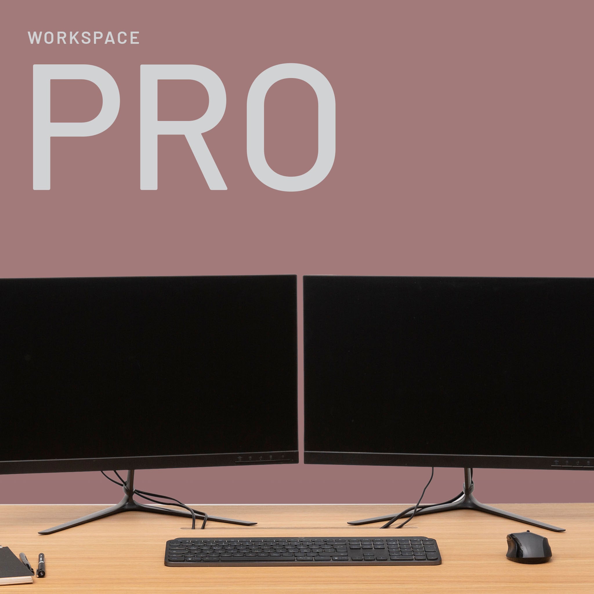 A minimalist workspace with two black monitors, keyboard, mouse, pen, and paper on a wooden desk. The mauve background and PRO branding set the stage for Fokus und Mission – der perfekte Ort zum Arbeiten.
