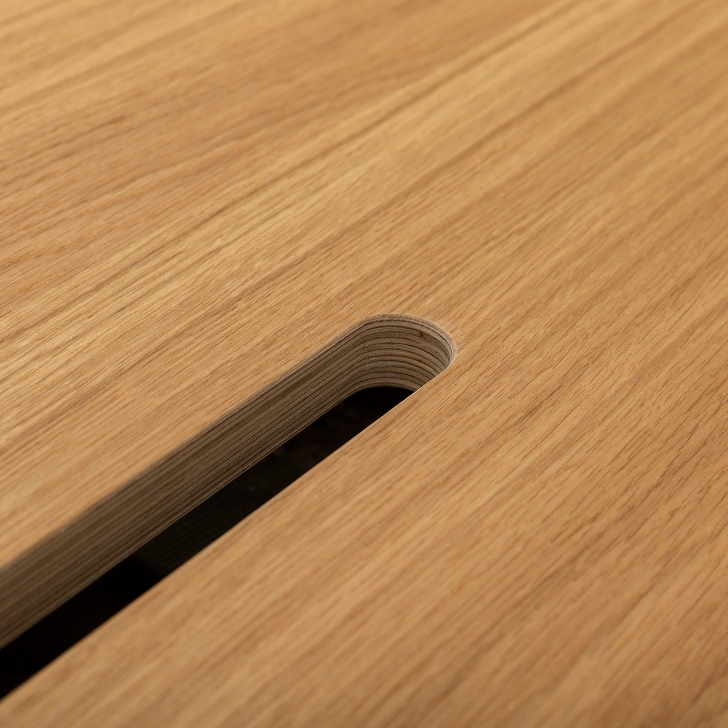 Close-up of the smooth, light surface of Kabeldurchlass - Oblong gefräst, featuring a rounded rectangular slot (Langloch) that displays layered wood edges and a dark space beneath.