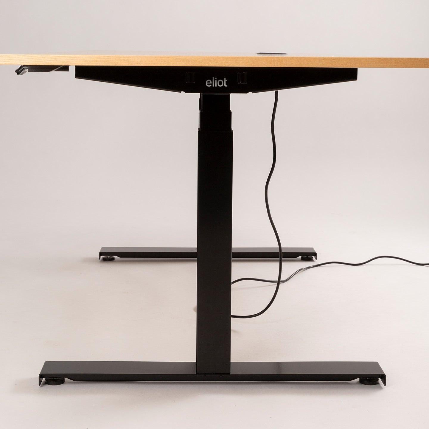 Der EXPAND-Schreibtisch von CUBE Products & Furniture verfügt über eine höhenverstellbare Holzplatte, schwarze Metallbeine und ein sichtbares Branding auf dem Rahmen. Darunter hängt ein freiliegendes Stromkabel, ideal für Hybrid-Arbeiter, die eine hochwertige Einrichtung suchen.