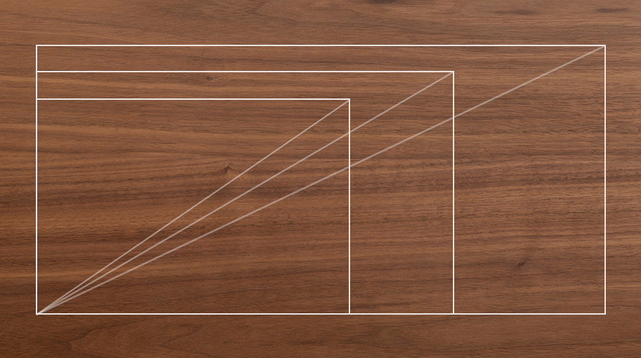Geometric white outlines of rectangles and diagonal lines overlap on a wooden surface, creating a minimalist, abstract design. The lines intersect at the bottom left corner of the image.