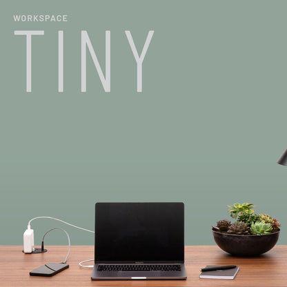A minimalist workspace featuring TINY—a laptop, phone, charger, notepad, desk lamp, and a bowl of succulents on a wooden desk—dein perfekter Begleiter und Organisator für den Alltag. Oben steht WORKSPACE TINY.