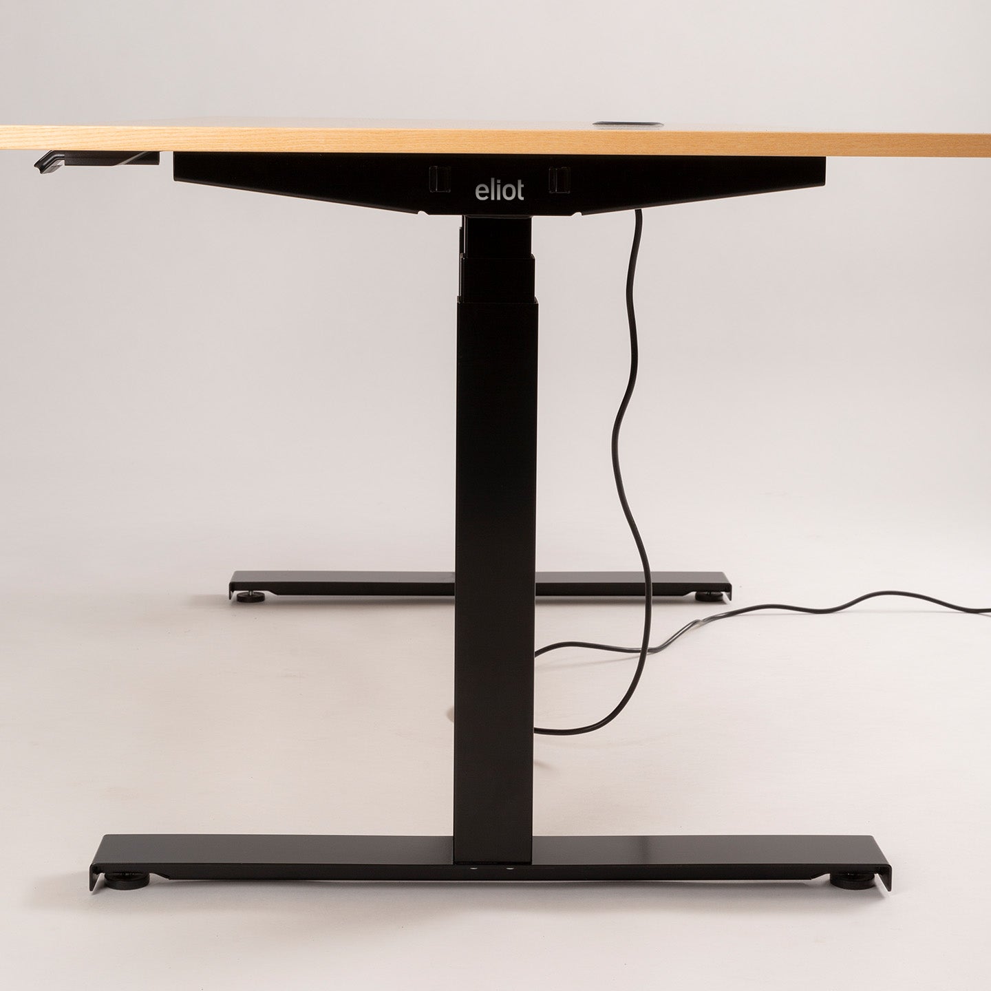 Der höhenverstellbare Tischgestell - Eliot Lock überzeugt mit Holzplatte, schwarzen Metallbeinen und Desk-Panel samt Kabelmanagement. Das eliot-Logo am Rahmen wird vor schlichtem, hellem Hintergrund präsentiert.