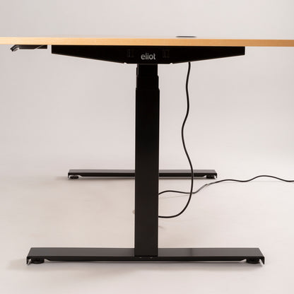 Der höhenverstellbare Tischgestell - Eliot Lock überzeugt mit Holzplatte, schwarzen Metallbeinen und Desk-Panel samt Kabelmanagement. Das eliot-Logo am Rahmen wird vor schlichtem, hellem Hintergrund präsentiert.