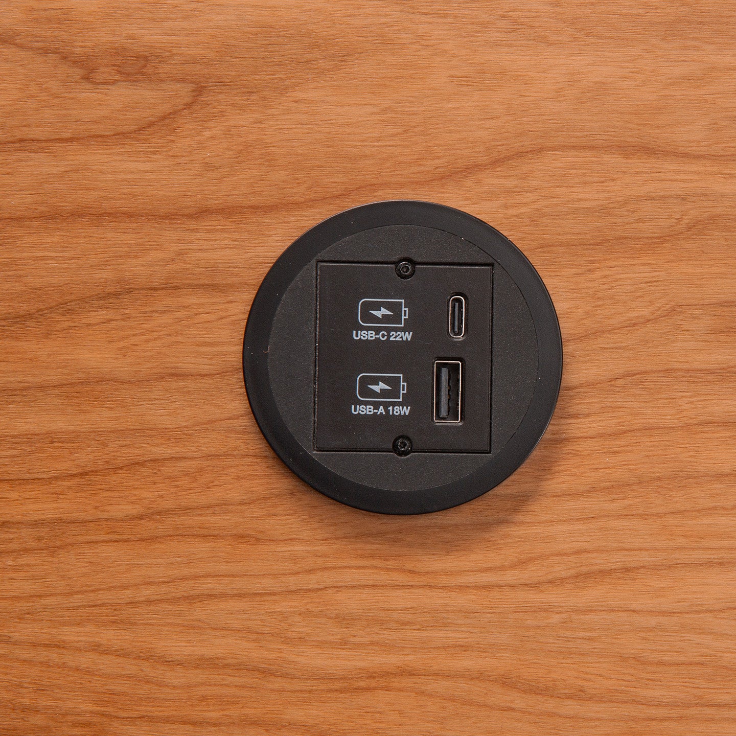 The Kombicharger USB A/C is a round, black, wood-embedded power outlet panel with integrated charging: USB-C (22W) and USB-A (18W) ports for convenient device charging.