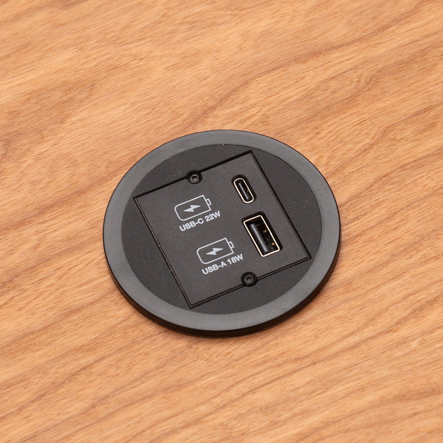 Eine Nahaufnahme eines CUBE Products & Furniture Kombicharger USB A/C mit eingebautem rundem Modul auf einem Holztisch, mit einem 22W USB-C Power Delivery-Anschluss und einem 18W USB-A-Anschluss.