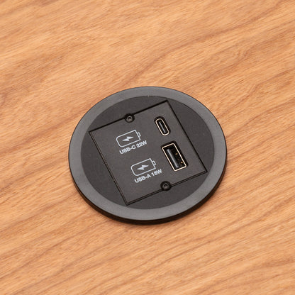 Eine Nahaufnahme eines CUBE Products & Furniture Kombicharger USB A/C mit eingebautem rundem Modul auf einem Holztisch, mit einem 22W USB-C Power Delivery-Anschluss und einem 18W USB-A-Anschluss.