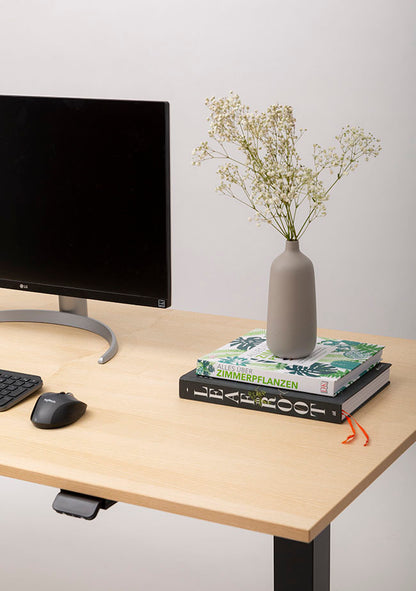 Create a minimal Home Office workspace with FLEX—a black monitor, keyboard, mouse, two books, and a gray vase with white flowers on a light wood desk—offering easy plug-and-play setup against a simple background.