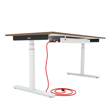 A modern adjustable-height Eliot desk with a dark wooden top, white metal legs, and a visible red power cord plugged into a Kabelwanne - 1 Cable PRO coiled on the floor. The desk features "elliot" written on the side for a sleek touch.